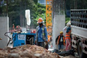 Workers at a construction site conducting a plate bearing test with equipment and materials like gravel, rebar, and a crane.